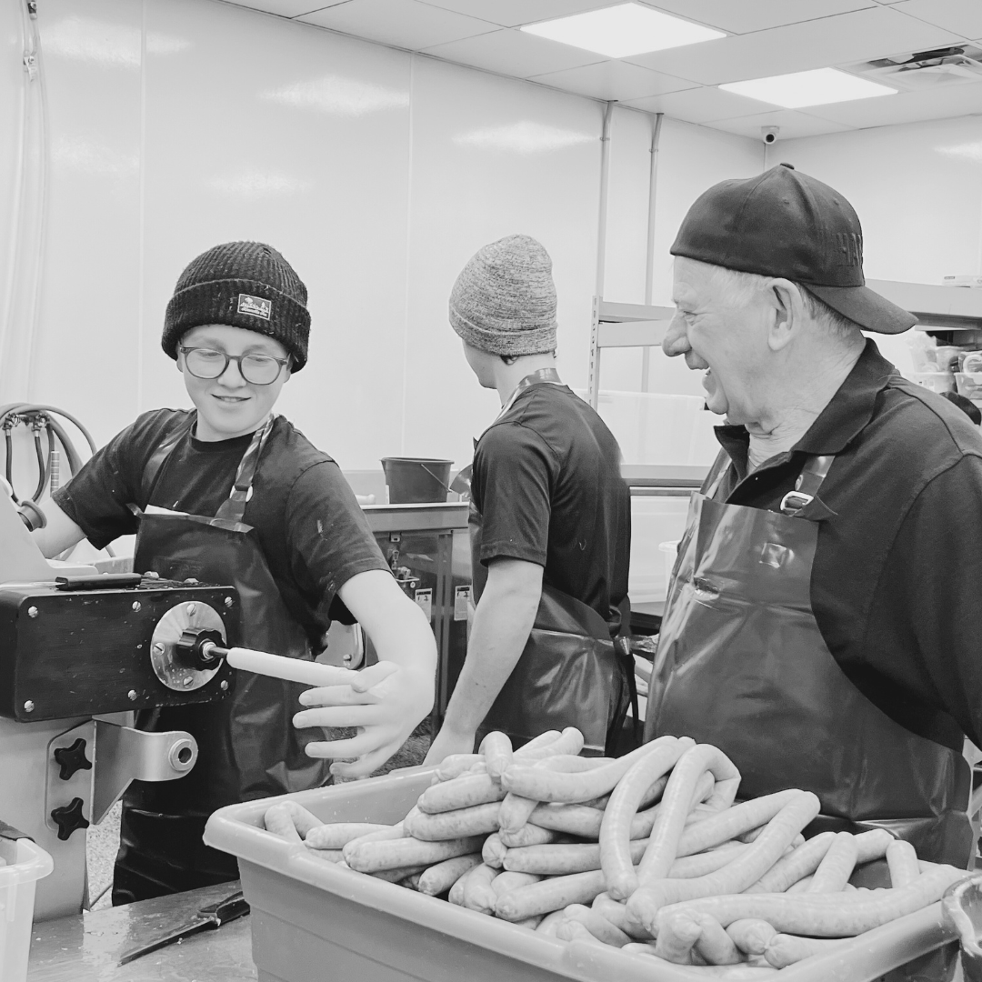 Workers in a sausage production facility preparing and packing fresh pepperoni meat by hand, showcasing a traditional approach to meat processing.